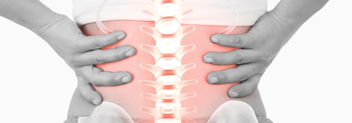 Medical illustration of hands placed on the lower back with a highlighted spine and red pain area.